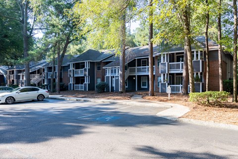 A white car is parked on the street in front of apartment buildings.