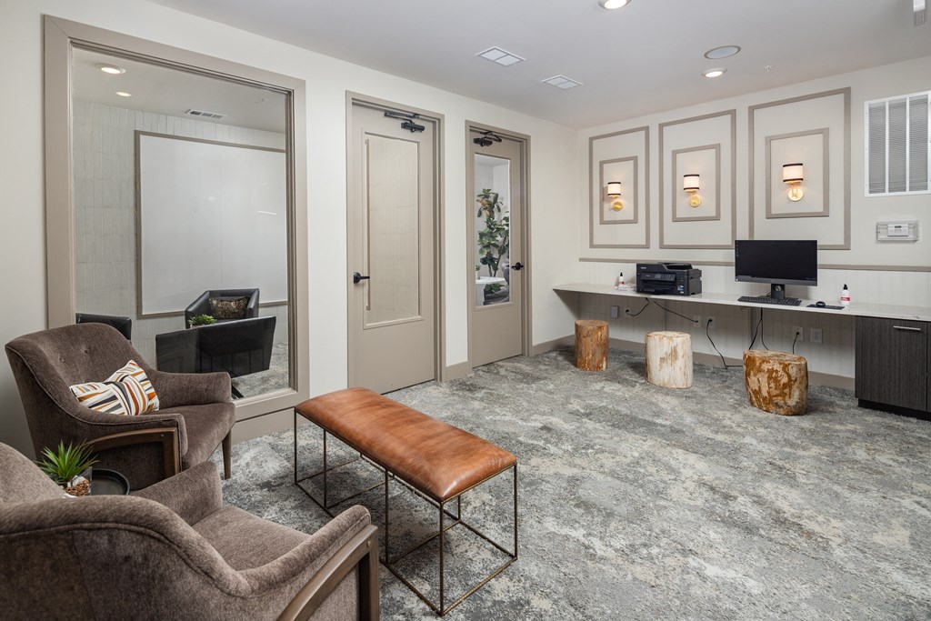 a living room with gray carpeting and a gray desk with a computer and a brown leather at The Flats at Southlawn Apartments, Lawrenceville