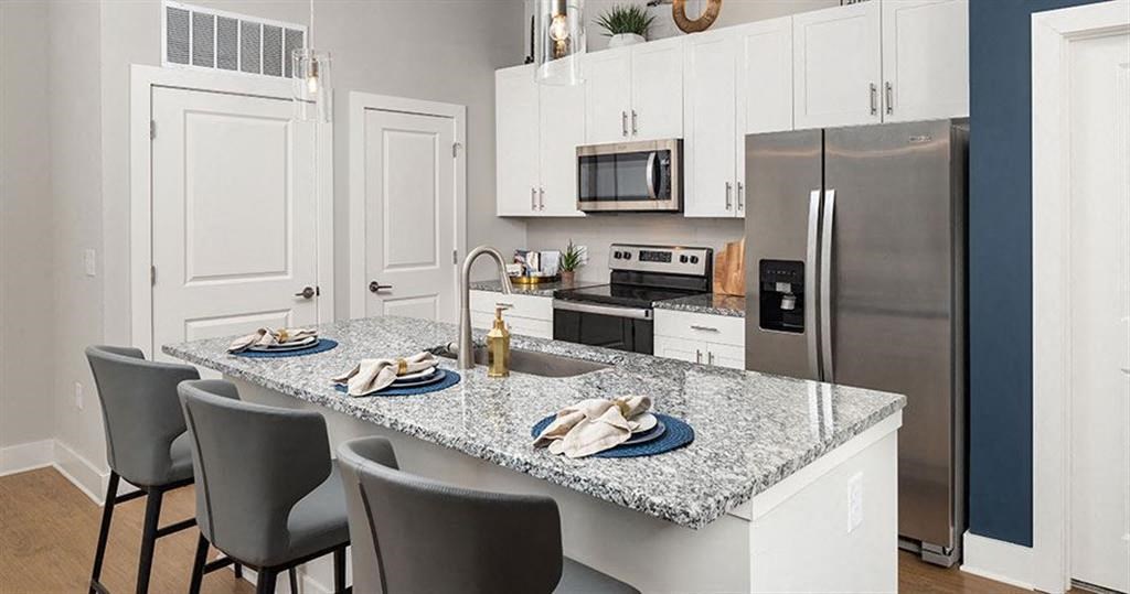 a kitchen with a marble counter top and a stainless steel refrigerator at The Flats at Southlawn Apartments, Lawrenceville, GA