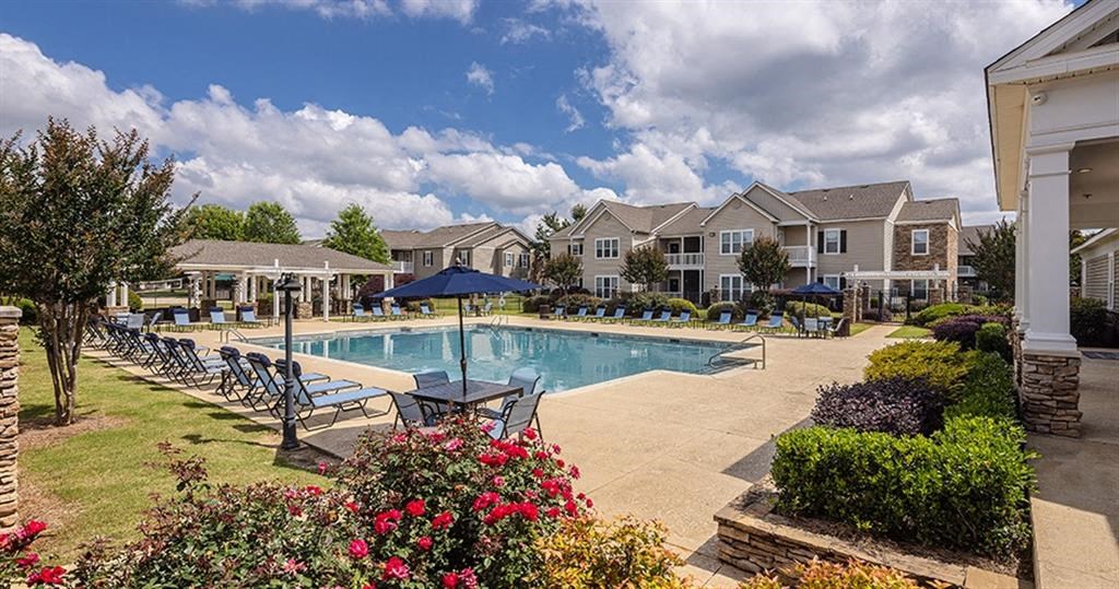 a swimming pool with chairs and umbrellas in front of houses at Bedford Parke Apartments, Warner Robins, GA