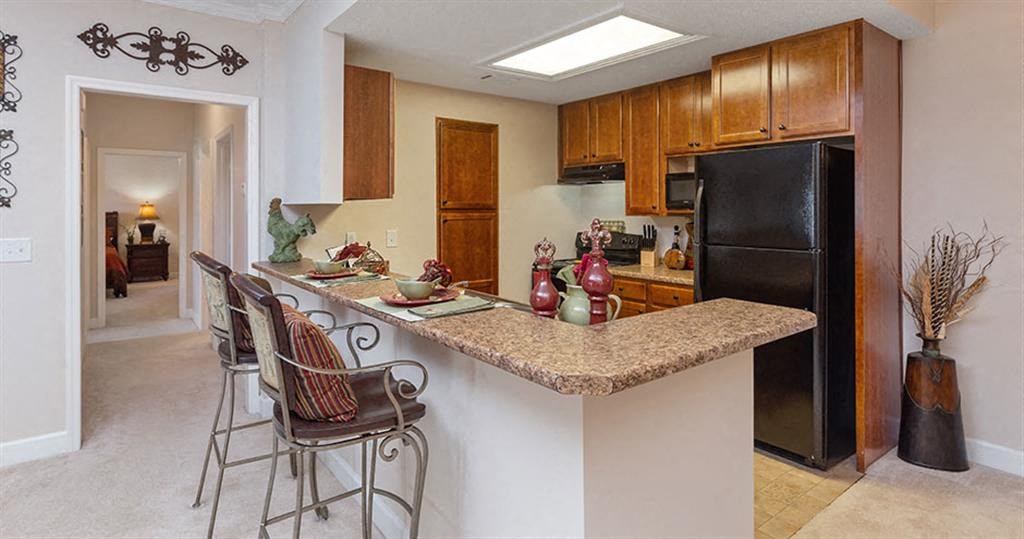 a kitchen with a bar with three chairs at Bedford Parke Apartments, Warner Robins, GA