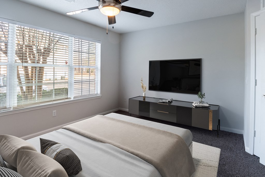 A bedroom with a bed, a television, and a window with blinds