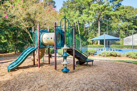 A playground with a green slide and a blue umbrella in the background.
