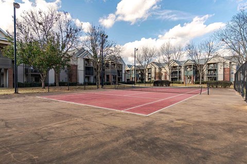 A tennis court is surrounded by apartment buildings.