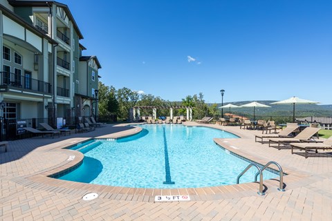 A large outdoor swimming pool surrounded by a brick patio and lounge chairs.
