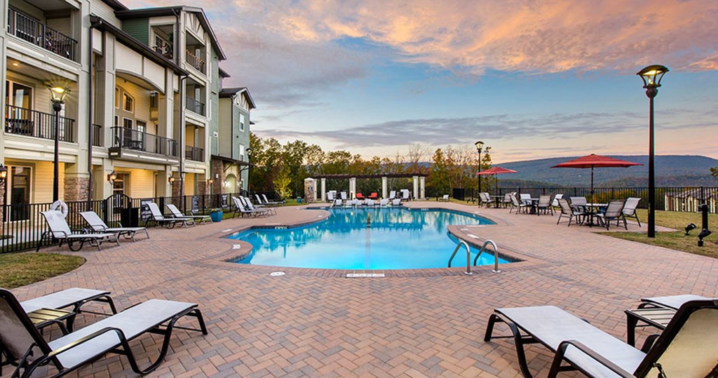 a swimming pool with chairs and umbrellas next to a building a swimming pool with chairs and umbrellas next to a building at Integra Vista Apartments, Hixson, TN