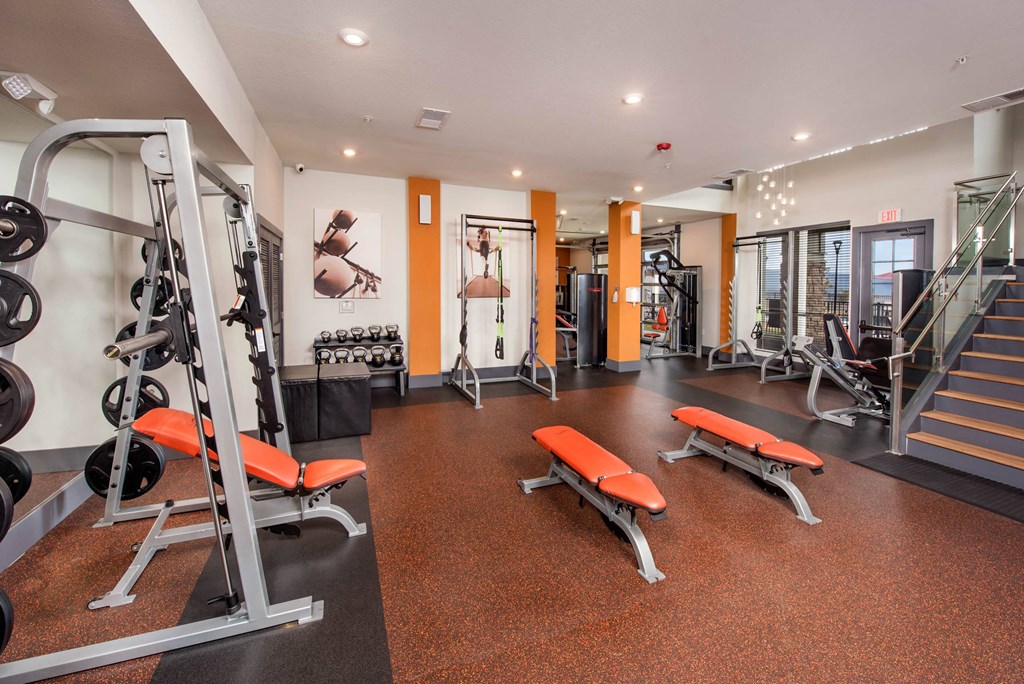 a gym with weights and cardio equipment on the floor and a staircase