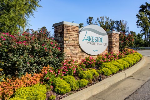 A sign for Lakeside Riverwatch stands in front of a flower bed.