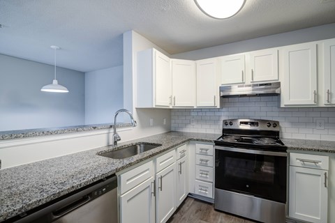 A kitchen with a stove, sink, and cabinets.