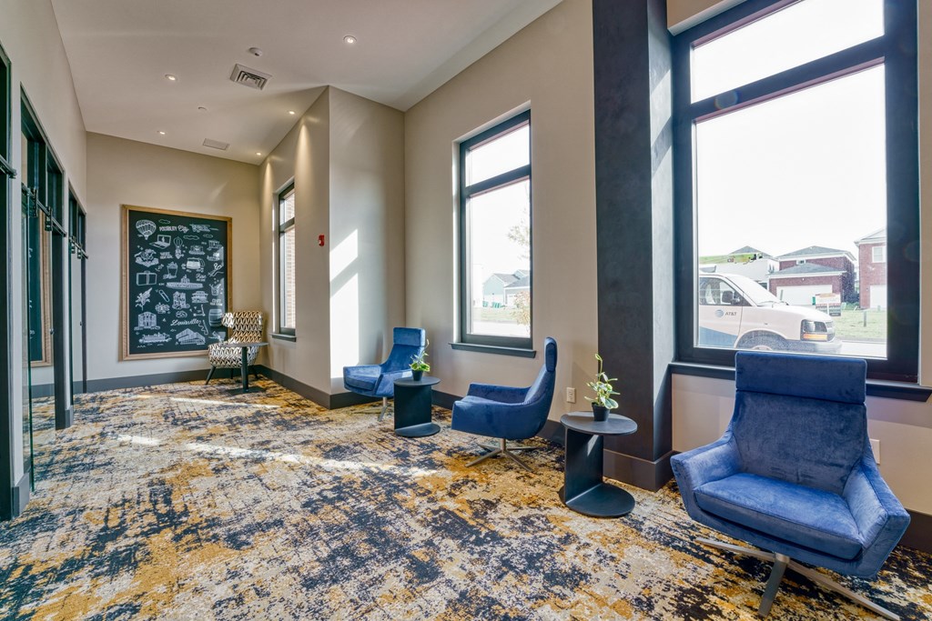 a lobby with blue chairs and a chalkboard on the wall and three large windows at Lyric at Norton Commons Apartments, Prospect, 40059