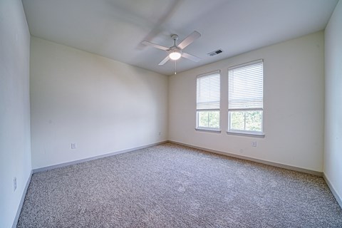 A room with a ceiling fan and two windows.