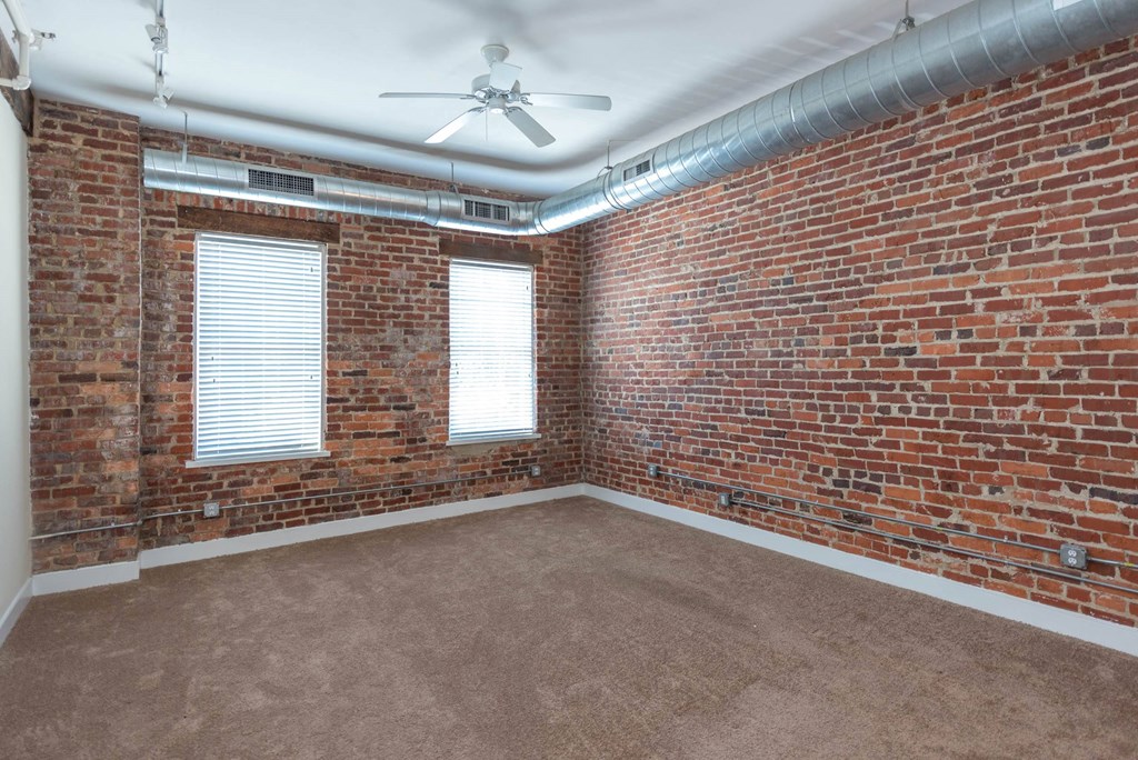 an empty room with a brick wall and a ceiling fan at Mayton Transfer Lofts, Petersburg, 23803