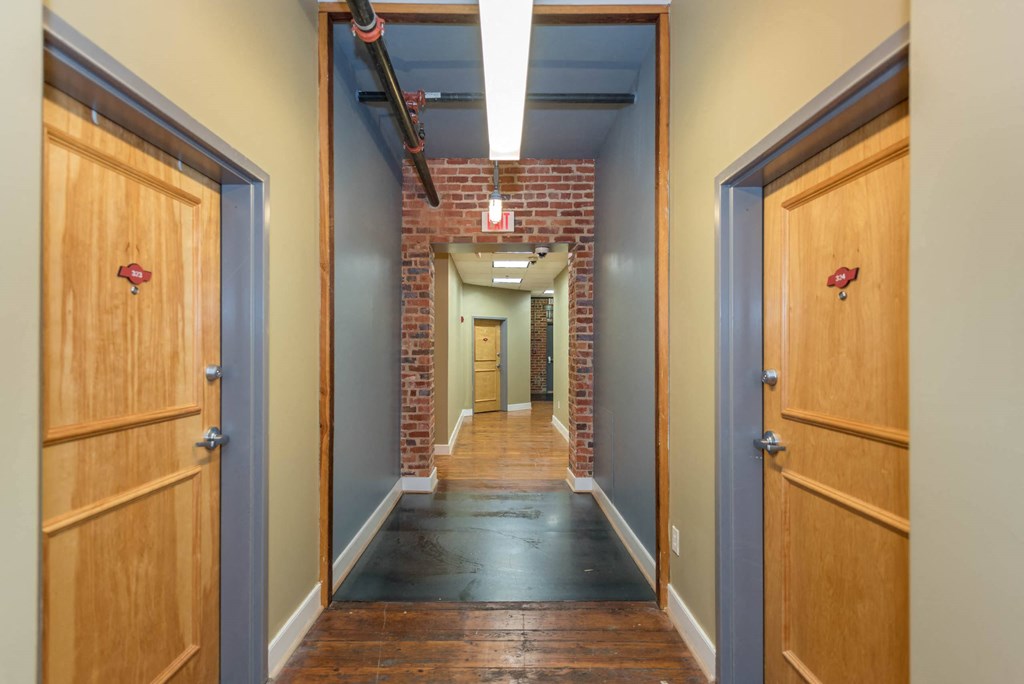 a hallway with wooden doors and a brick wall at Mayton Transfer Lofts, Petersburg, VA