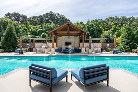 A pool with a wooden pavilion and lounge chairs.