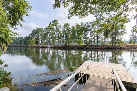 A dock extends into a calm body of water with trees in the background.