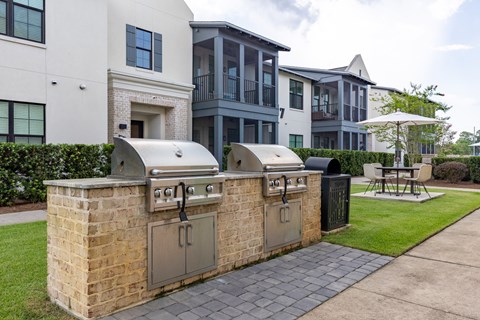 A brick BBQ grill is in front of a white and grey apartment building.