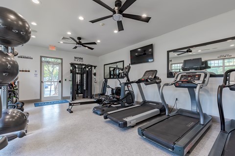 A spacious gym with treadmills, elliptical machines, and a ceiling fan.
