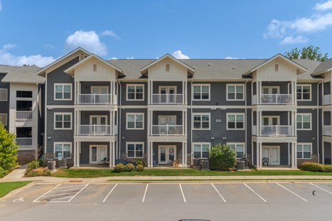 Apartment building with grey and white exterior and a parking lot in front.