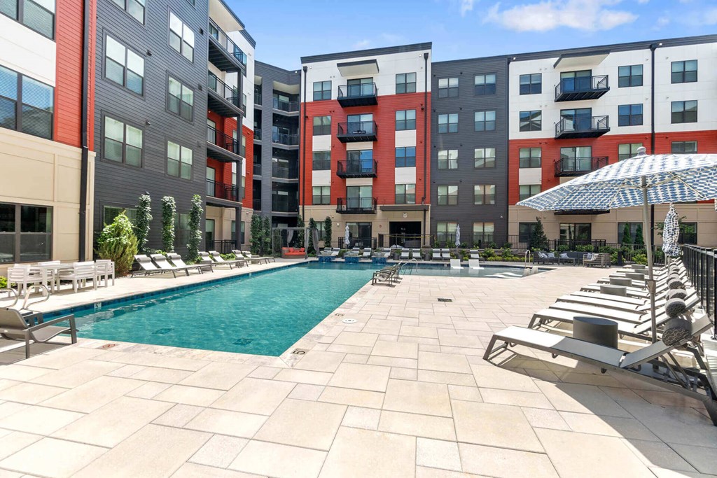 a swimming pool with chaise lounge chairs and umbrellas in front of an apartment building at Tapestry West, Richmond, VA
