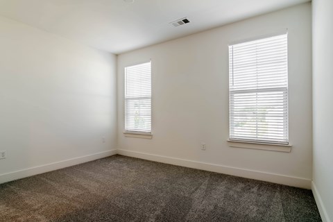A room with carpeted floor and two windows.