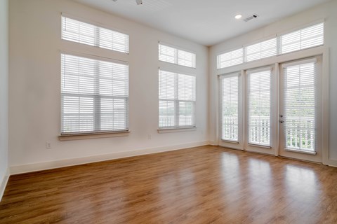 A room with wooden floors and three windows with blinds.
