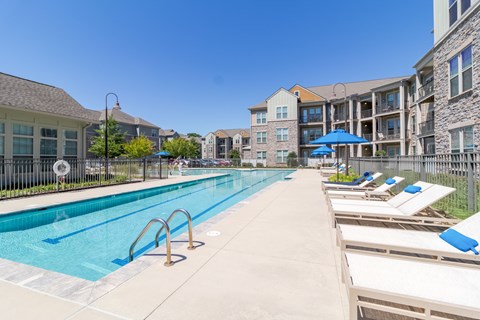 A swimming pool with sun loungers and apartment buildings in the background.