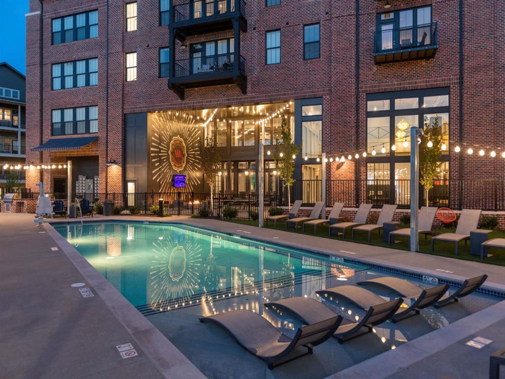 a swimming pool with chaise lounge chairs and a brick building in the background at Livingston Flats Apartments, Chesterfield
