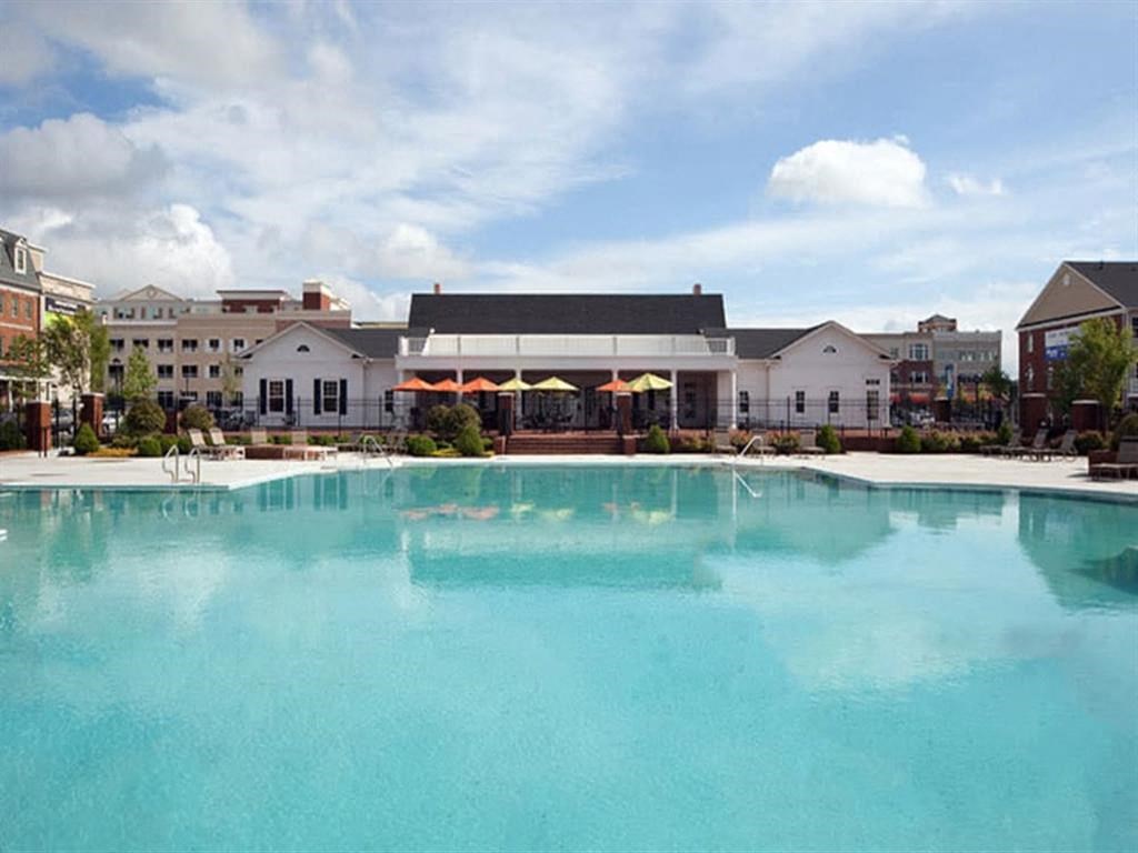 a large pool with umbrellas and buildings in the background at Flats at West Broad Village, Glen Allen, VA