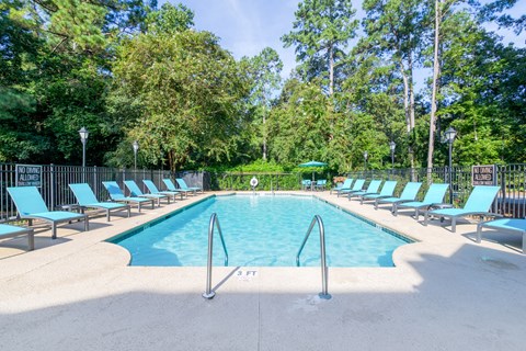 A large swimming pool surrounded by trees and lounge chairs.