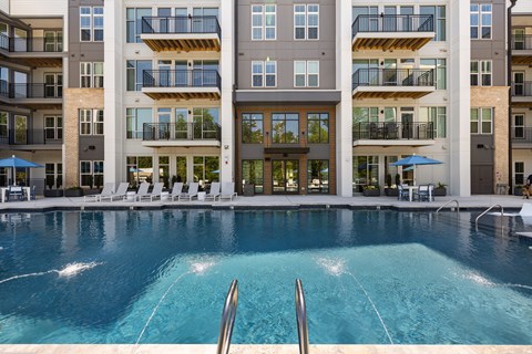 A large swimming pool in front of a multi-story apartment building.
