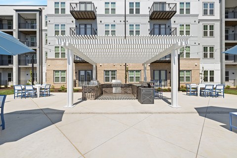 A patio with a white pergola and blue chairs is surrounded by apartment buildings.