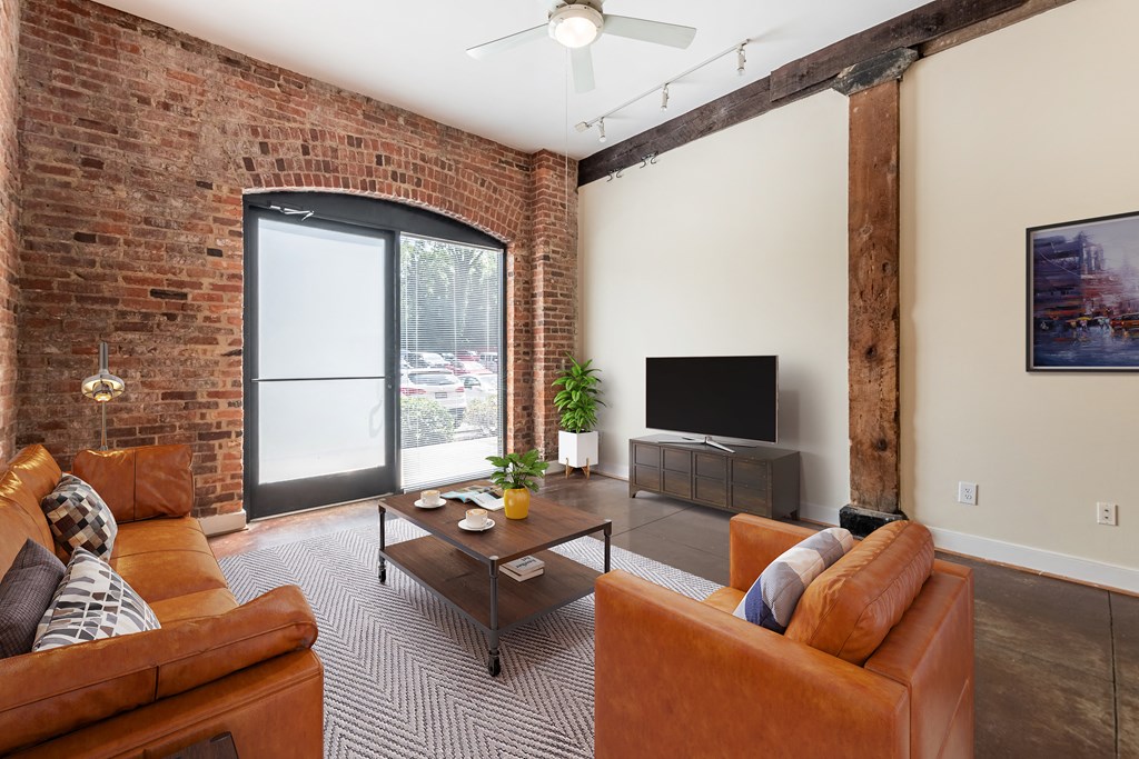 a living room with leather furniture and a brick wall at Mayton Transfer Lofts in Virginia 23803