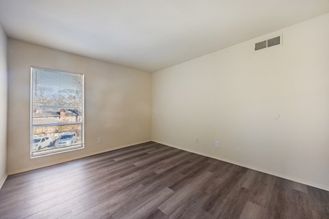 A room with wooden flooring and a window showing a parking lot outside.
