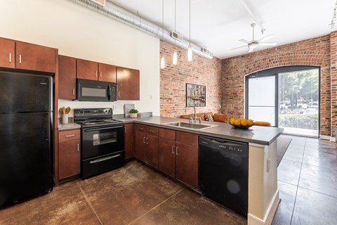 a kitchen with black appliances and wooden cabinets and a brick wall