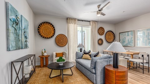 A living room with a grey couch, a black table, and a painting on the wall.