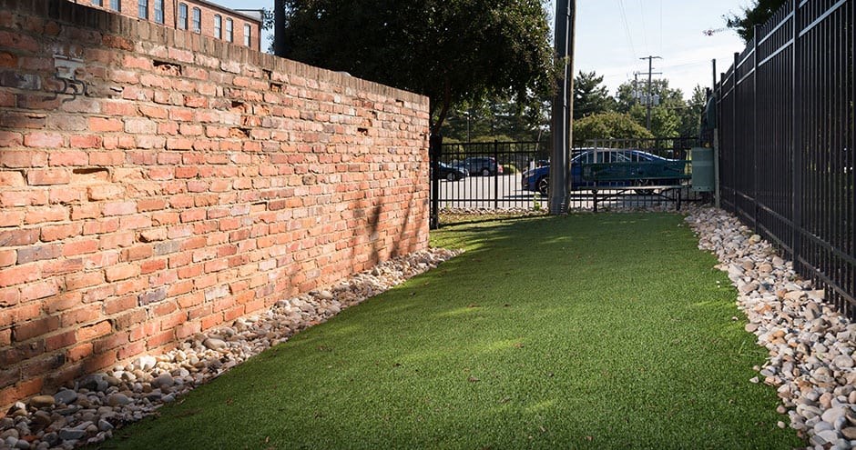a brick wall and a yard with green grass at Mayton Transfer Lofts, Petersburg, VA 23803