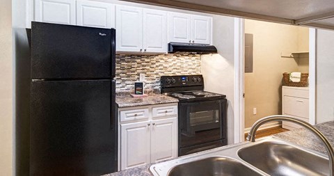A black refrigerator is in a kitchen with white cabinets at Austin Chase Apartments, Macon