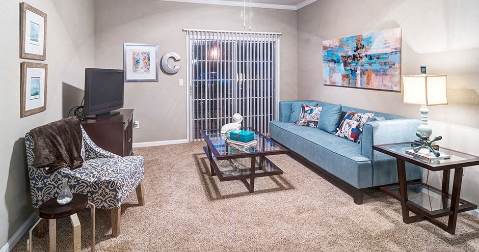 A living room with a blue couch, a chair with a blanket, a coffee table, and a television at Austin Chase Apartments, Macon, 31210