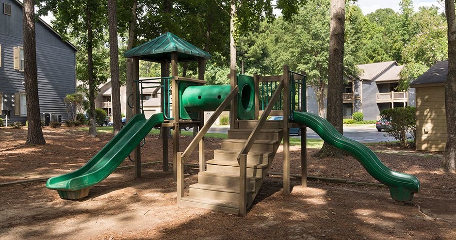 A playground with a green slide and a wooden structure A playground with a green slide and a wooden structure at Austin Chase Apartments, Georgia