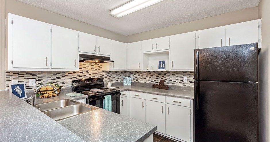 A kitchen with white cabinets and a black refrigerator.