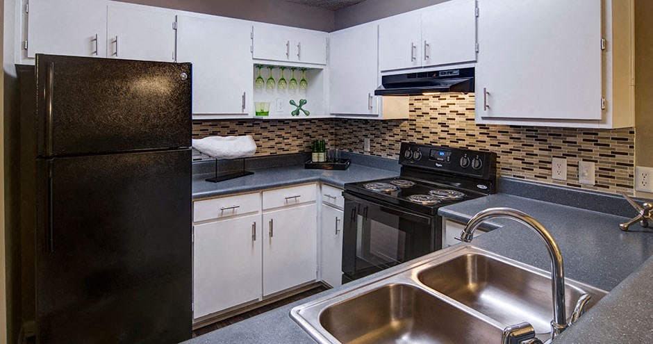 A black refrigerator stands next to a sink in a kitchen.