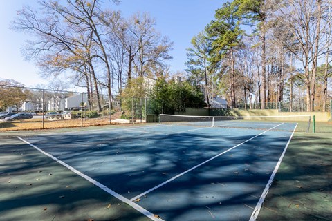 A tennis court surrounded by trees and a fence.
