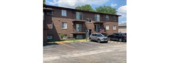 A parking lot in front of a brown brick apartment building with two cars parked.