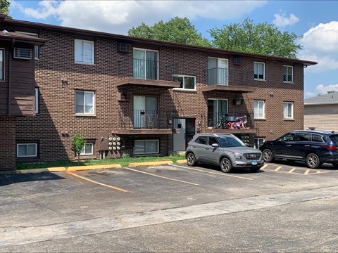 A parking lot in front of a brown brick apartment building with two cars parked.
