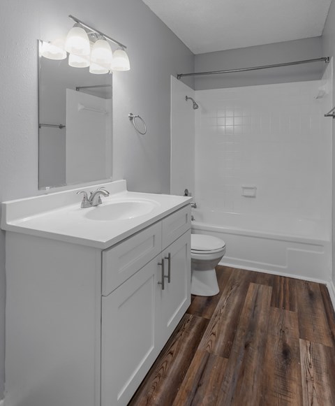 A white bathroom with wood flooring and a white sink.