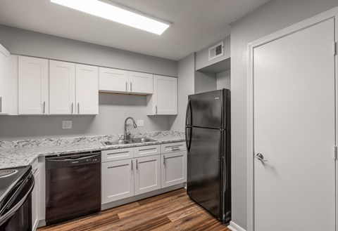 A kitchen with a black refrigerator and white cabinets.