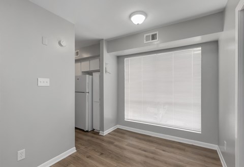 A kitchen area with a refrigerator, cabinets, and a window with blinds.
