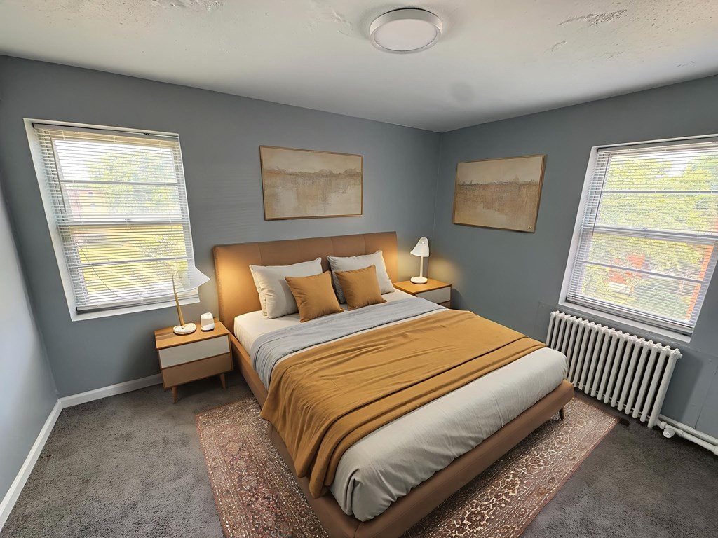 A bedroom with a bed, nightstands, and two windows.