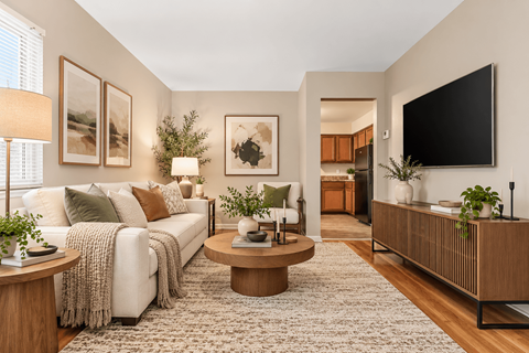 A living room with a white couch, a coffee table, and a flat screen TV mounted on the wall.
