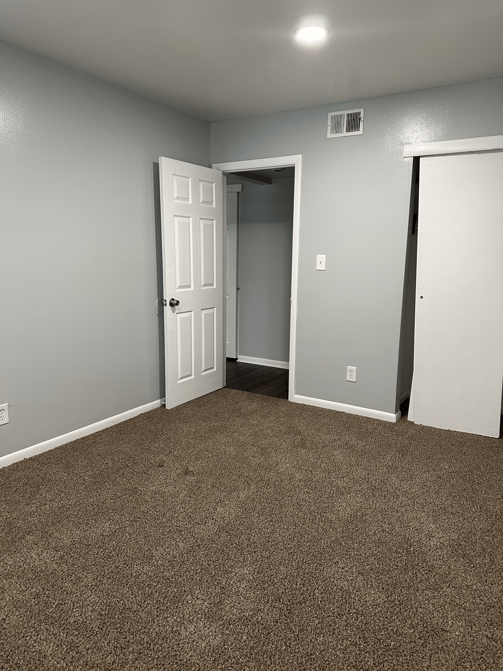 A room with a carpeted floor and two doors, one of which is open.
